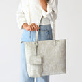 Woman wearing a white button-up shirt and light blue jeans carrying a cream floral jacquard tote bag with matching pouch and keychain.