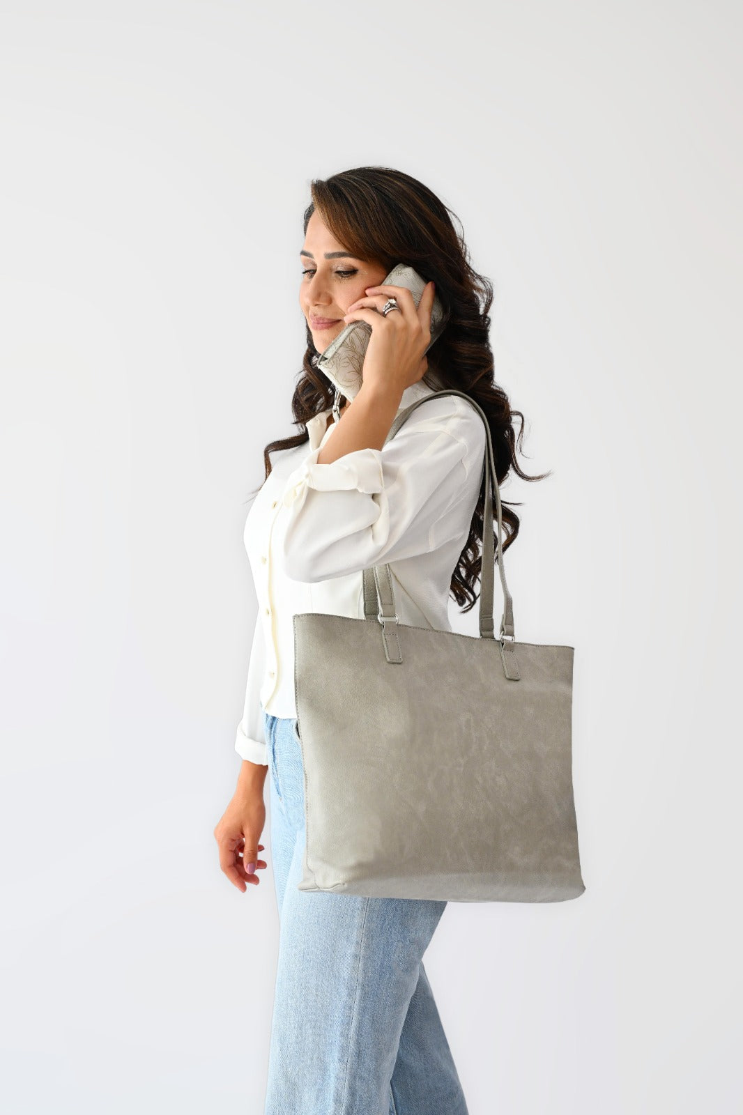 Woman wearing a white button-up shirt and light blue jeans carrying a cream floral jacquard tote bag with matching pouch and keychain.