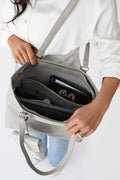 Woman wearing a white button-up shirt and light blue jeans carrying a cream floral jacquard tote bag with matching pouch and keychain.