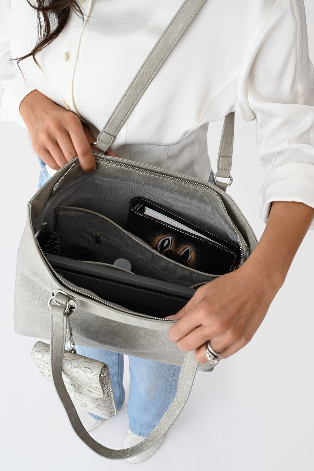 Woman wearing a white button-up shirt and light blue jeans carrying a cream floral jacquard tote bag with matching pouch and keychain.